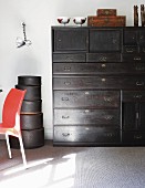 Antique, black chest of drawers next to stacked hatboxes against white wall