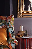 Colourful reading chair next to small side table with reflective top; gilt-framed mirror above on wall