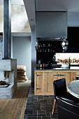 Open-plan interior with black brick floor and wooden kitchen cupboards; concrete open fireplace to one side