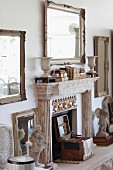 Fireplace with moulded mantel flanked by antique sculptures on hearth and below framed mirror on wall