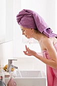 Frau mit Badetuch bekleidet und Handtuch auf dem Kopf wäscht sich im Badezimmer