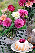 A table in the garden set with a Bundt cake, summer flowers and a hurricane lamp