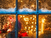 Blick durch vereistes Fenster auf Christbaum und Weihnachtsgeschenke