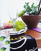 Wine glass and chrysanthemum flower on place setting next to plant in wooden bowl
