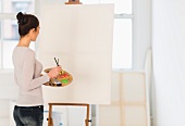 Woman standing in front of blank canvas on easel in artist's studio