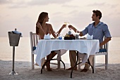 Couple toasting each other with glasses of champagne and enjoying a romantic dinner on the beach