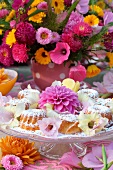 Farbenfroher Sommerblumenstrauss vor festlicher Etagere mit frischem Gebäck und prachtvoller Dahlie