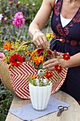 Woman arranging summer flowers in vase on garden table