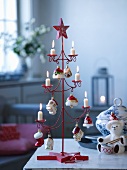 Stylised, red metal Christmas tree with lit candles and toys on table