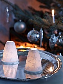 Tealights under porcelain covers with star motifs on silver tray in front of Christmas tree