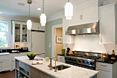 White country-house kitchen with island below traditional pendant lamps