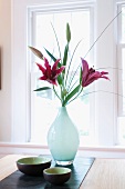 Pink lilies in glass vase and Japanese dishes on bamboo runner in front of window