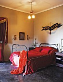 Original, romantic decor in bedroom - ceiling light with cherub and artwork with lettering reading 'Heaven's gate' on wall combined with metal bed and red velvet bedspread
