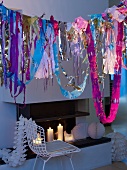 Garlands hanging above white wire chair in front of fireplace with lit candles and decorative honeycomb paper balls