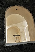 View of modern metal table in austere vaulted interior with niches seen through arched window