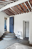 Concrete steps leading to blue wooden door and rustic exposed roof structure in purist bedroom
