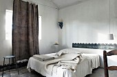 Various blankets on French bed, casual linen curtain hung from taut wire and sheet metal bands as borders on wall