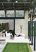 Lady reading on a sofa on a terrace in front of a custom home with exposed concrete walls and lightweight metal roof