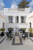 North African style courtyard with black and white theme with wicker chairs around a mosaic table and potted palms
