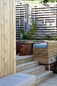 Bench made of wooden laths on split-level terrace and trellising on stone wall