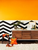 Orange colour gradient on wall above black and white zigzag dado as dynamic background for designer sideboard