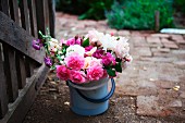 White and pink, cottage-garden bouquet in plastic bucket next to garden gate