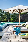 Cushioned sun loungers and sun umbrella on a wooden deck by a swimming pool