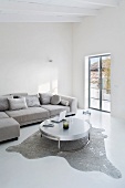 Purist living room in grey and white with designer table on animal-skin rug and corner sofa