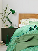 Bett mit Kopfteil aus Holz und gemustertem Plaid neben Nachtkästchen mit grüner Retro Tischlampe