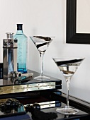 Liqueur glasses and metal cocktail shaker on a glossy, black surface