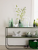 Bottles and crockery on retro shelves made from curved metal in front of a white wall