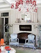 Silver gilt, antique armchairs with shimmering upholstery and chandelier with red crystals in front of open fireplace