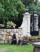 Two dogs in front of stone wall and wrought iron garden gate with decorative masonry pillars