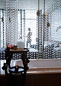 Chain curtain screening bathtub from bedroom; toiletries on carved wooden table