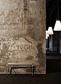 Designer metal bench against concrete wall in repurposed factory hall; view into hallway with white, conical pendant lamps