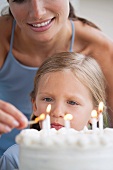Mother lighting the candles on her daughter's birthday cake