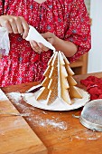Woman using piping bag to decorate Christmas tree of homemade gingerbread shapes