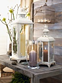 Lit candle in candle lantern in front of vintage-style lanterns on rustic wooden bench