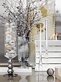 Christmas baubles in glass container, silver vase of decorated twigs next to candlesticks