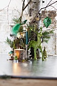 Green reindeer ornament and lit candle in front of tree trunk decorated with Christmas baubles