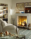 Open fireplace with tiled fireback in living room with white leather couch and maritime decor