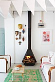 Vintage Couchtisch auf Teppichläufer und weiße Sofagarnitur vor schwarzem Kaminofen mit Feuer, im Vordergrund weiße Wimpelkette