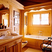 Waschtisch mit Unterschrank aus Massivholz neben Badewanne am Fenster im Bad eines Holzhauses