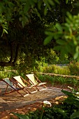 Deckchairs with fabric seats on wooden deck in garden in evening sun