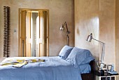 Double bed with pale blue bed linen and vintage lamps against marbled walls; half-open folding doors in background