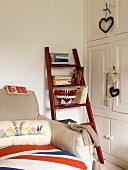 White fitted cupboards and a wooden ladder holding books, next to a sofa