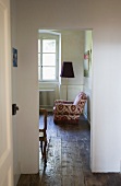 Chair upholstered with floral fabric next to a floor lamp in a guest room with wooden flooring in a former monastery
