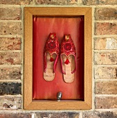 Orientalische Schuhe als Wanddeko in einem Holzrahmen an einer Ziegelmauer