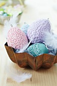 Various Easter eggs decorated with lace doilies and feathers in metal cake mould