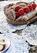 Crocheted doilies tied together as mat on stone underneath wooden board of bread and vine tomatoes